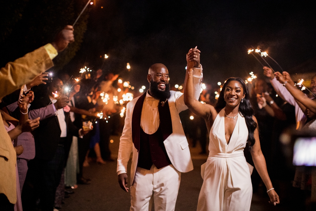 Bride and groom walking hand in hand through a sparkler exit at night