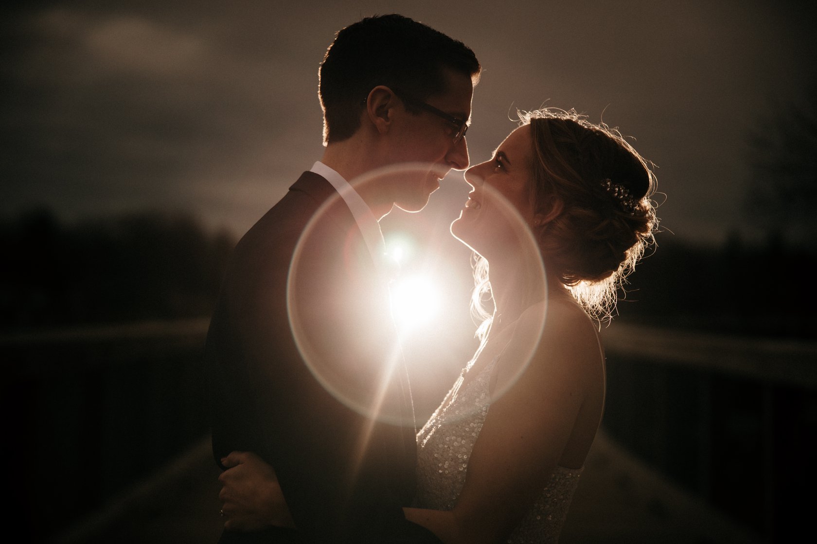 Bride and groom face each other as the halo from the background light highlights their smiles 