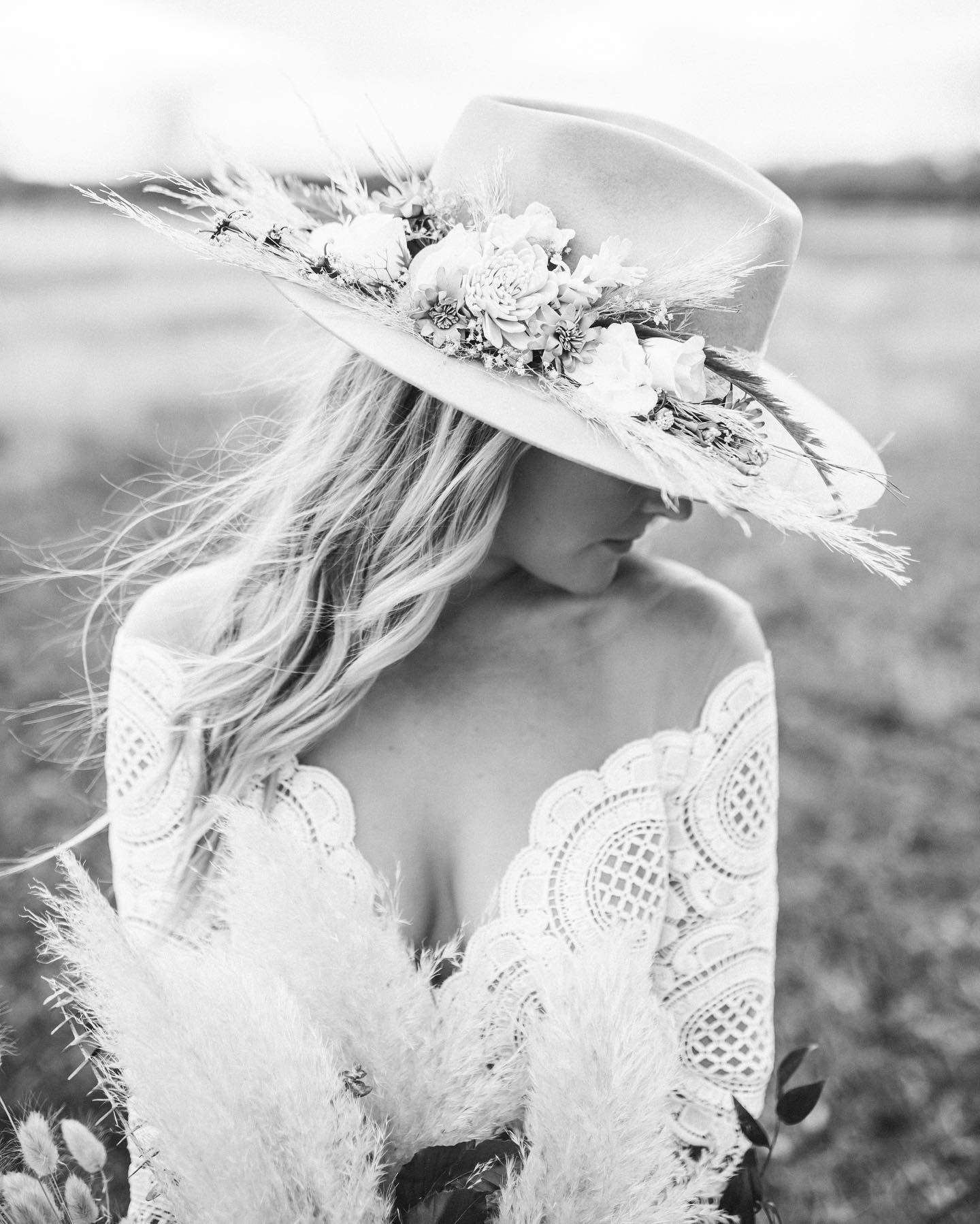 Black and white portrait of a bride facing sideways and wearing a floral fedora hat 