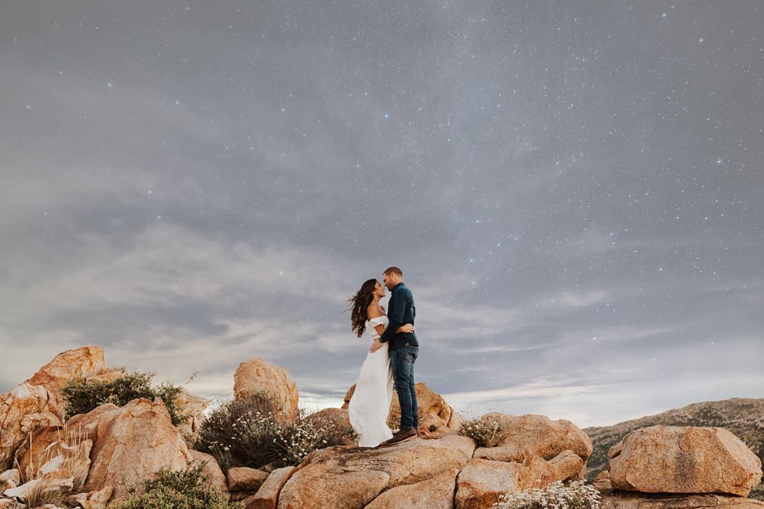 A couple holding each other as they pose standing on a rock with a starry sky background