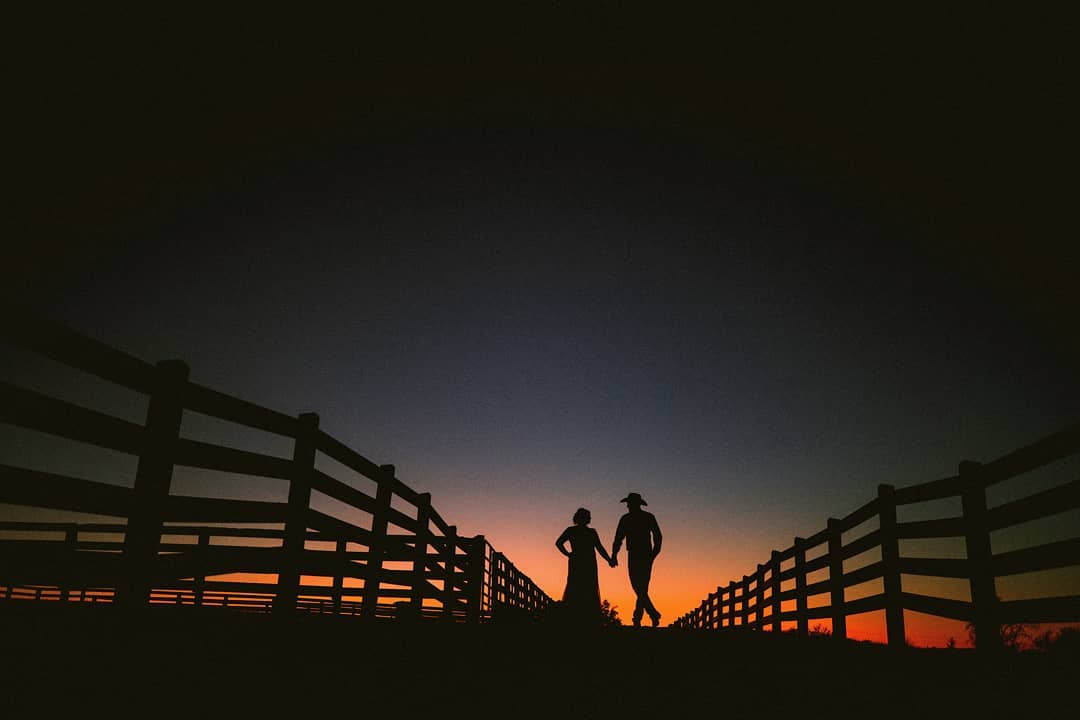 Silhouette of a couple posing on a field bordered with fences on either side