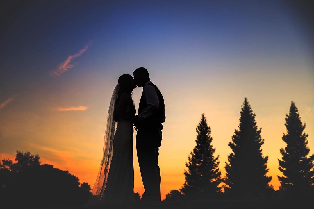 Silhouette of a bride and groom kissing and holding hands at sunset