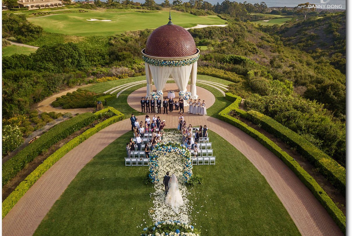 A bird's eye view of an outdoor wedding venue as a bride and groom walks down the aisle 