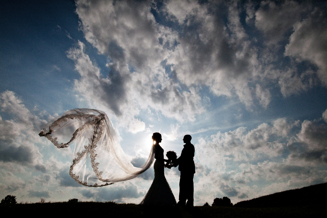 Silhouette of a bride and groom holding the bridal bouquet as the bridal veil toss mid-air
