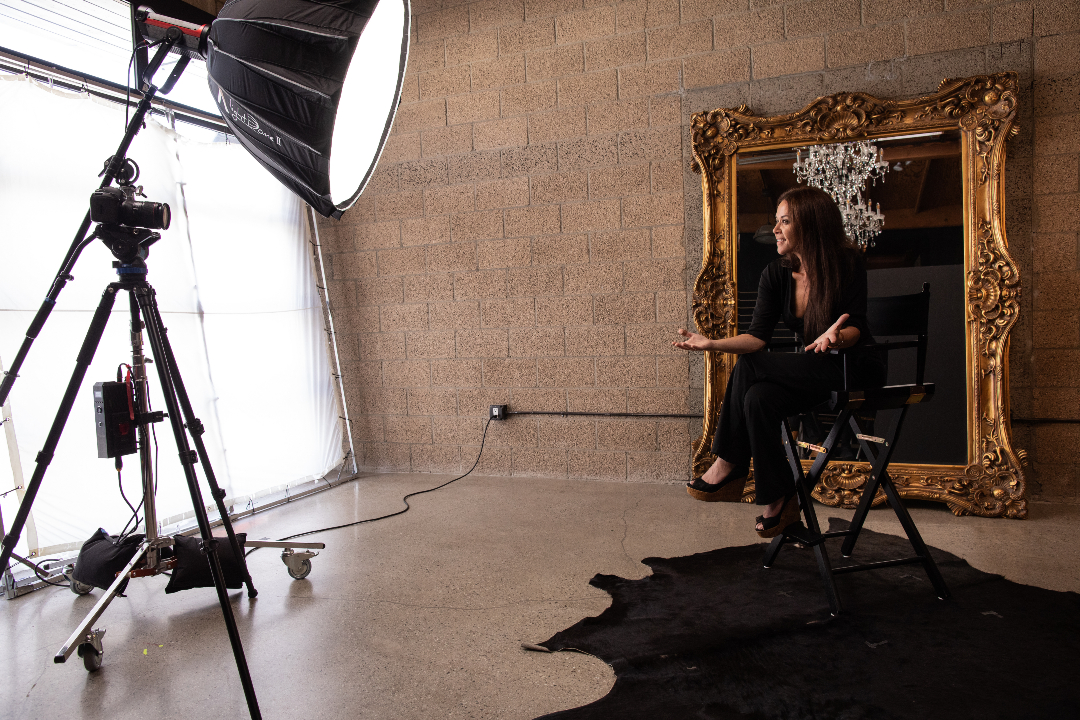 A women siting in front of a mirror while being recorded with lights positioned towards her