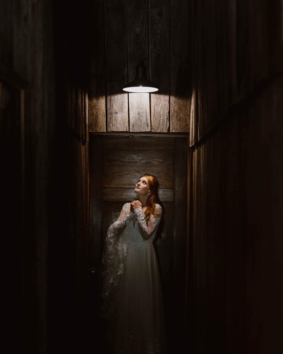 A bride standing in front of a dark doorway with a lit lamp at the top