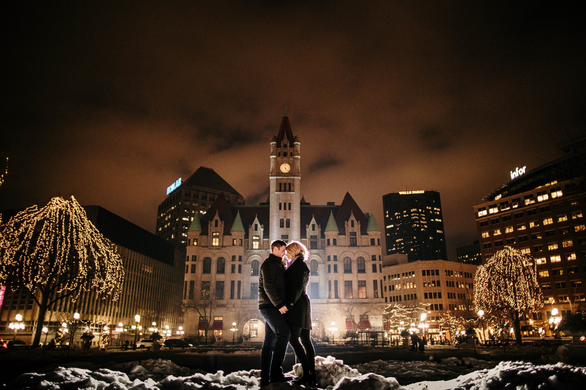 A couple standing in front of a clock tower during the night time while holding hands