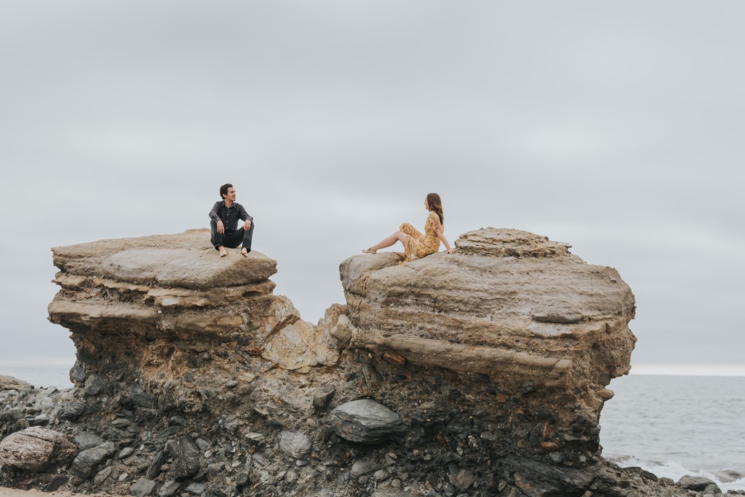 A couple posing while sitting on top of two different rocks