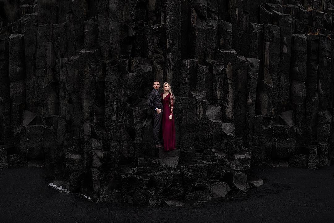A couple posing standing on a black-colored rock cliff for an engagement session