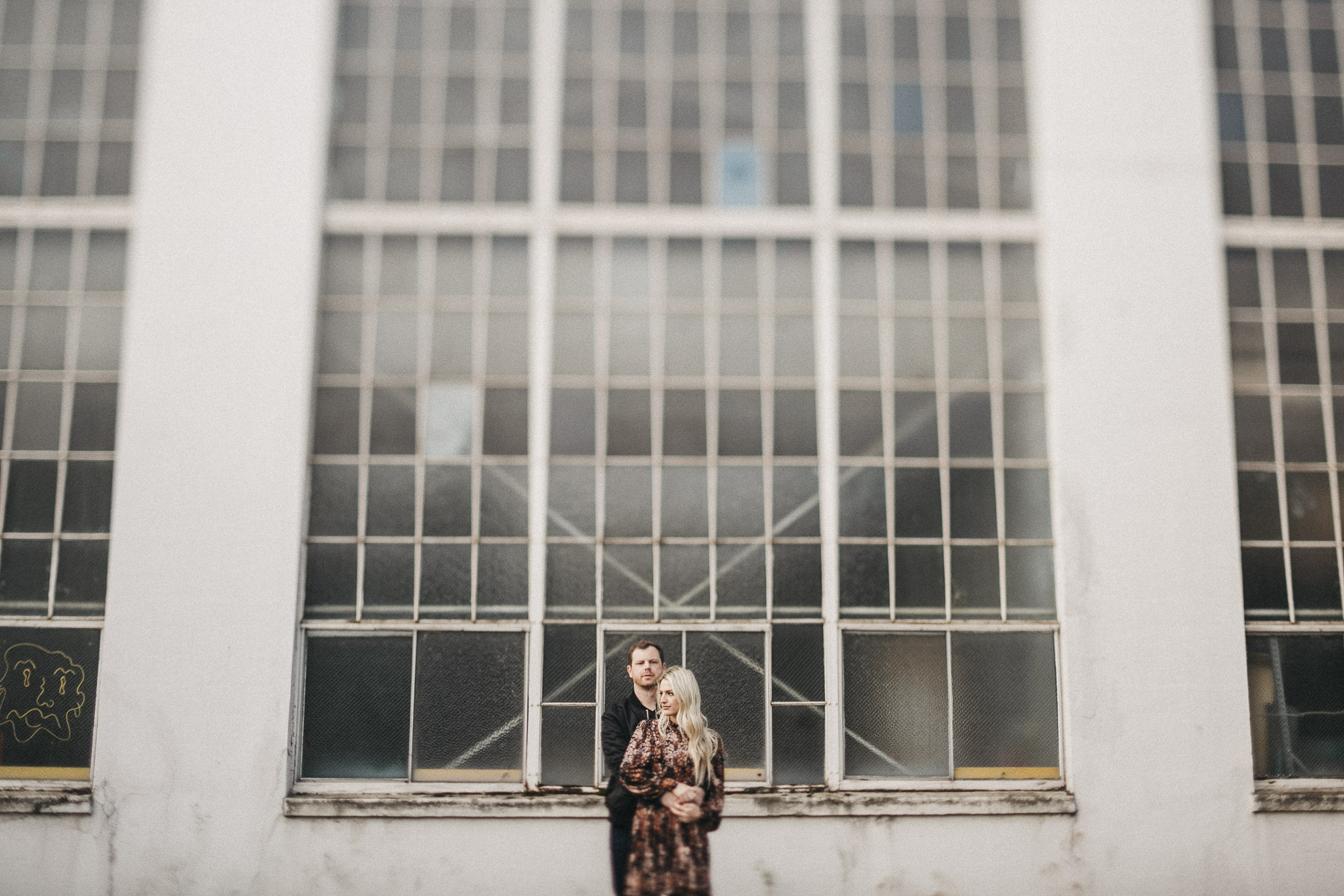 A couple portrait in front of a white wall with windows