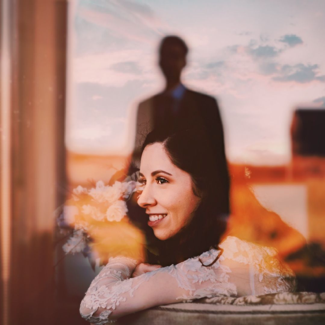 A bridal portrait through the window with the reflection of the groom's shadow 