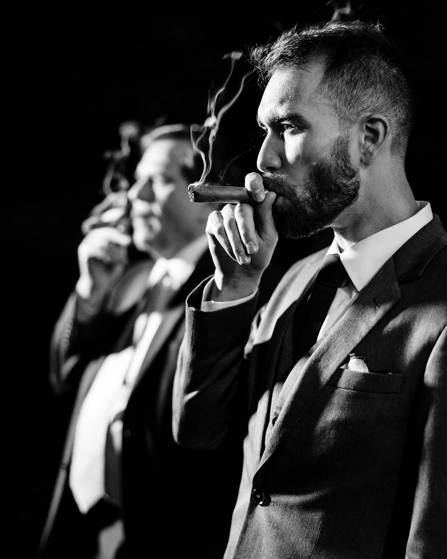A monochrome portrait of a groom smoking cigar