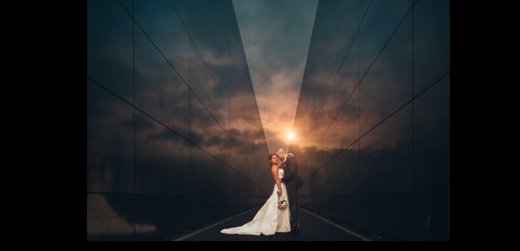 A bride and groom posing in front of a glass wall reflecting a sunset
