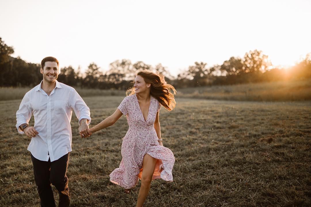 A couple running through a field smiling and holding hands 