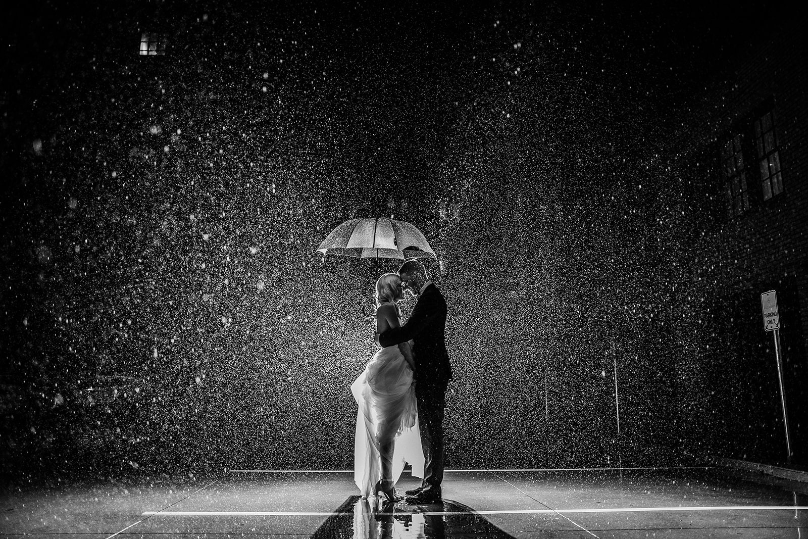 A bride and groom holding each other under an umbrella as it rains