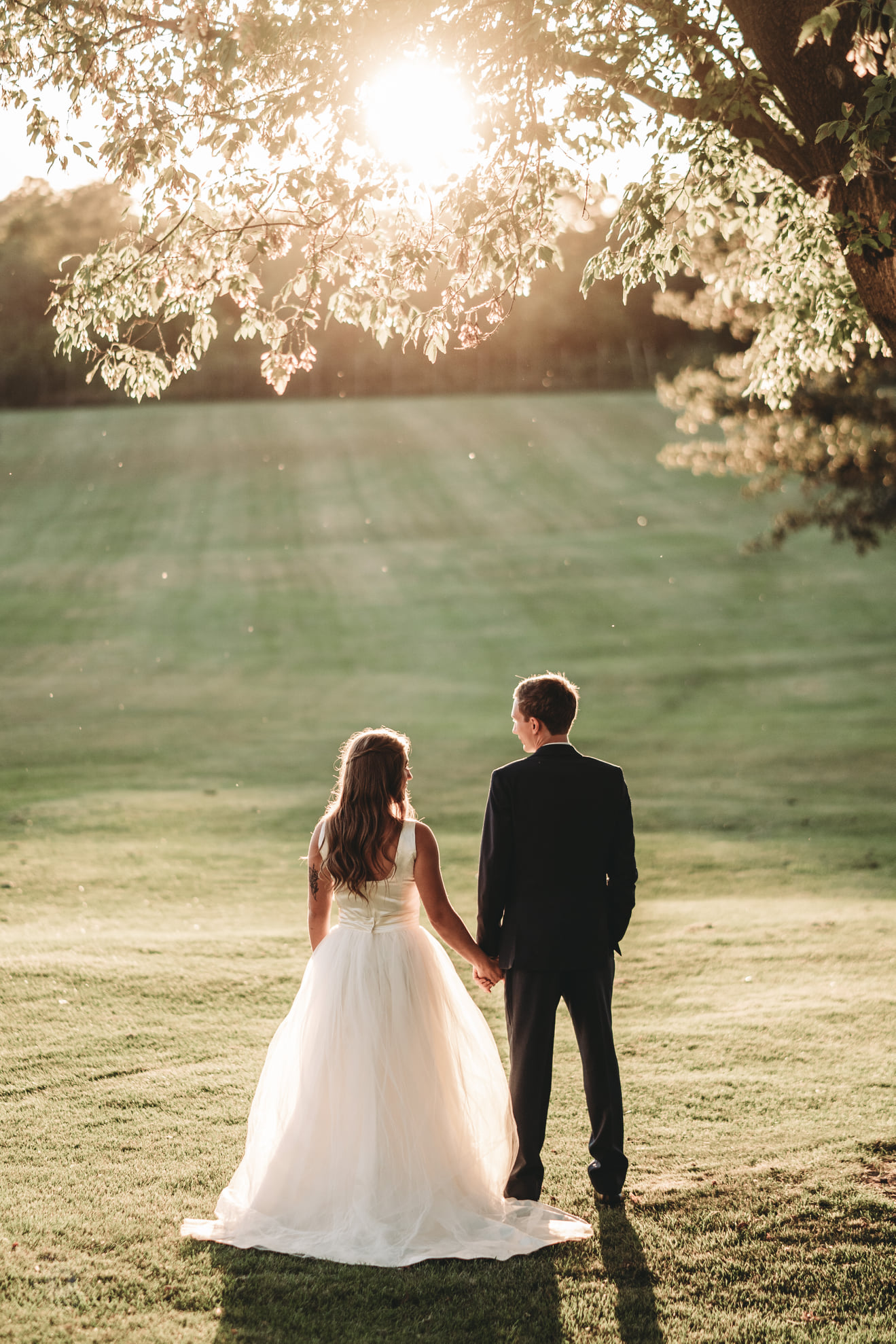 A wedding portrait of a bride and groom holding hands while standing under a tree 