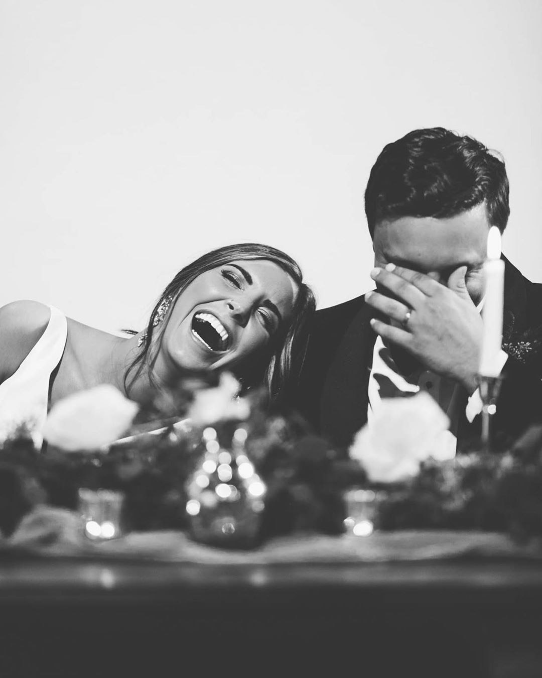 a married couple laughing with the bride's head on the groom's shoulder