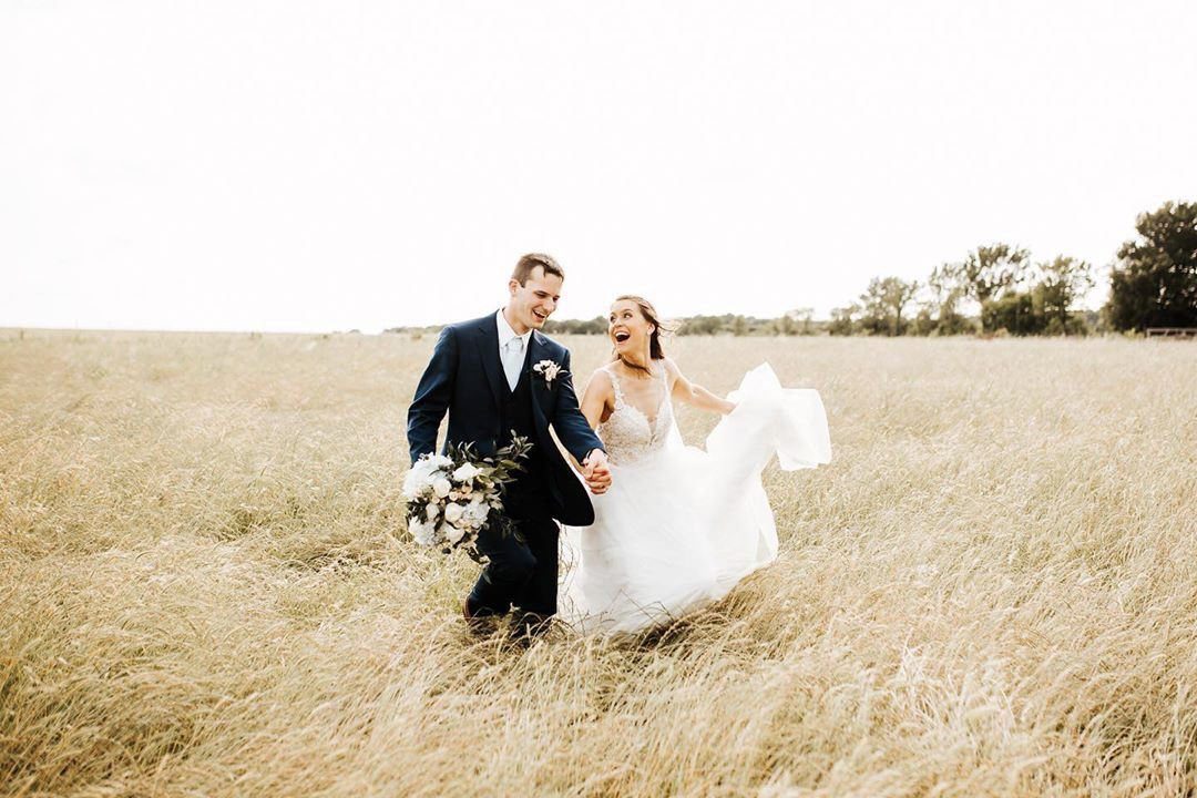 a married couple running through a grassy field in their wedding attire 