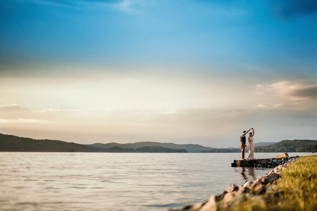 a couple standing by a beautiful lake under open skies 