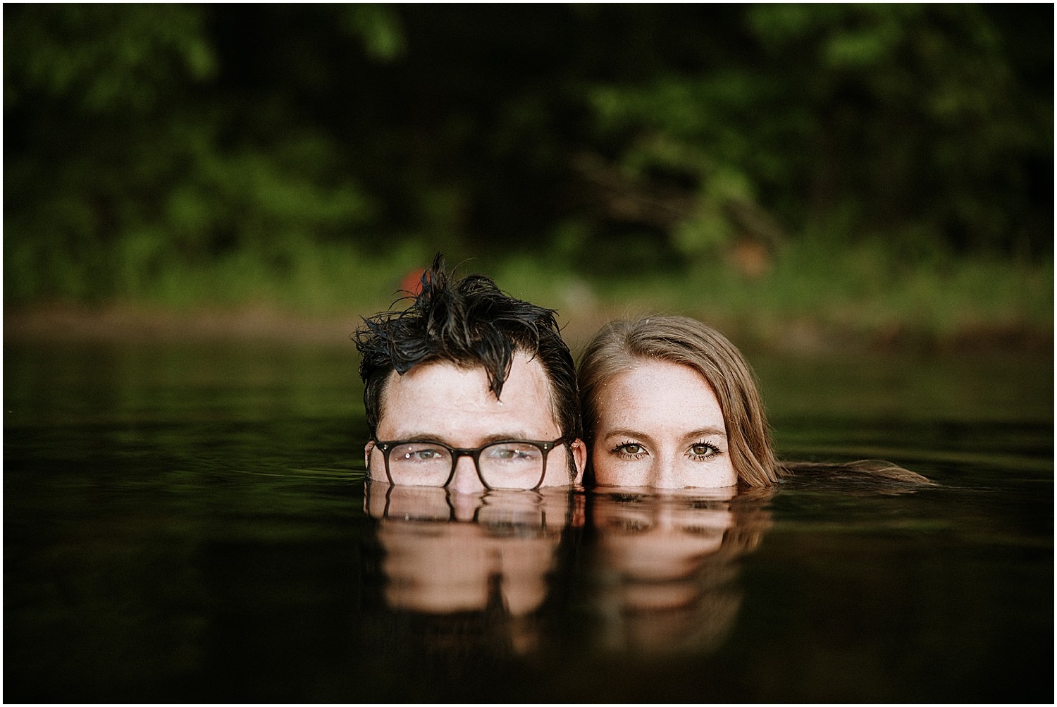 a couple looking at the camera while almost completely submerged in a lake