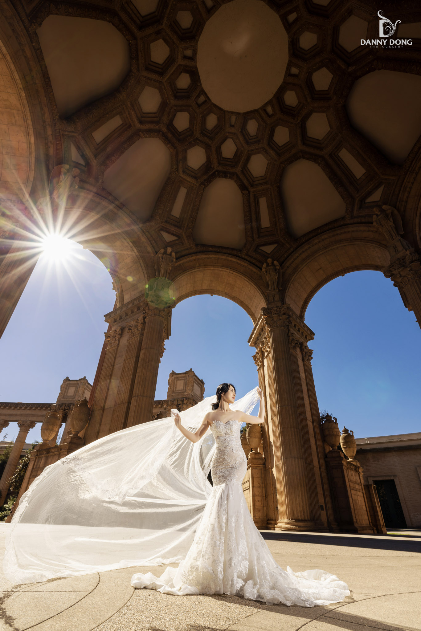 a bride in wedding attire in front of an arch with sun flares